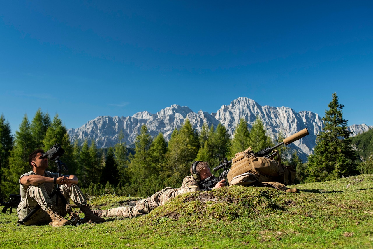 Soldiers aim a gun in the mountains.
