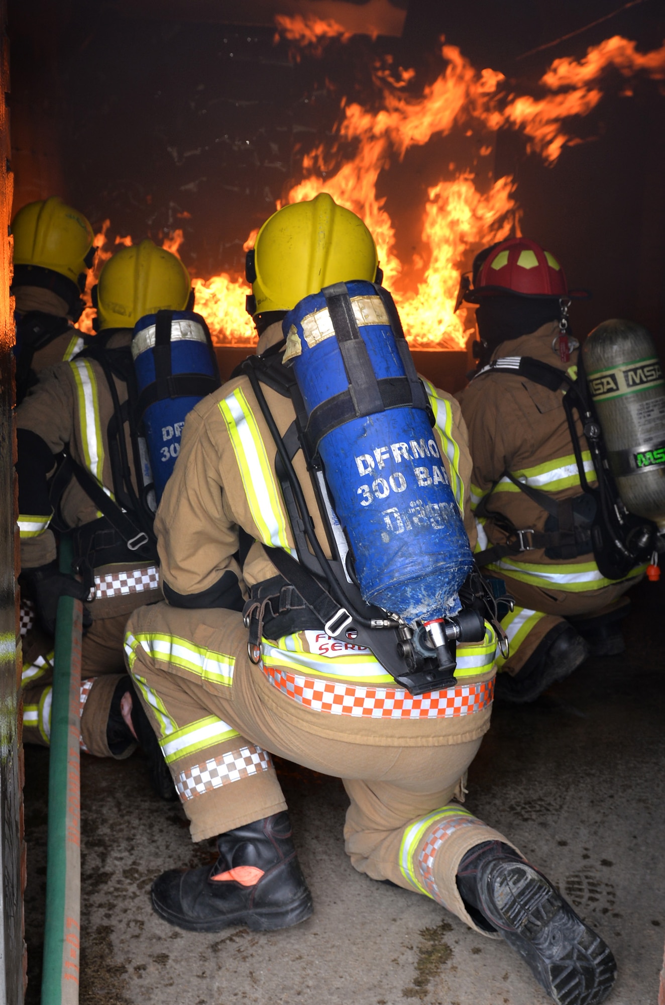 Royal Air Force firefighters from RAF Marham, Norfolk, kneel alongside U.S. Air Force firefighters as they put out flames in the live fire training house on RAF Mildenhall, England, April 5, 2019. The British fire crew visited the base to gain experience on the live fire trainer. With the arrival of the F-35 and the regeneration at RAF Marham, their training facilities are under renovation and the visit served to provide vital training for the RAF firefighters, and aid in continuing to build vital working relationships between RAF Mildenhall and neighboring fire departments. (U.S. Air Force photo by Karen Abeyasekere)