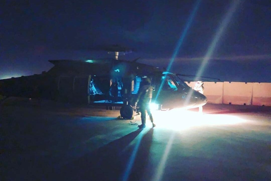 A helicopter sits on the ground at night with bright lights shining on the front of it.