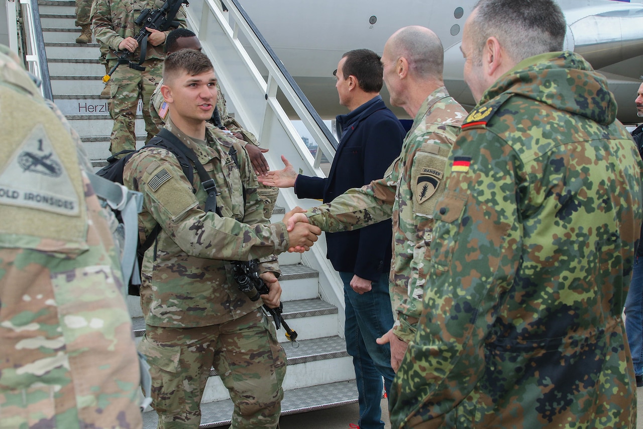 Soldiers exit an airplane and shake hands with other soldiers.