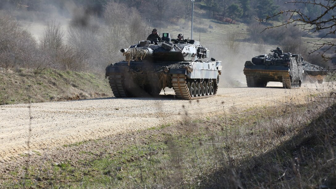 Tanks roll down a dirt road.