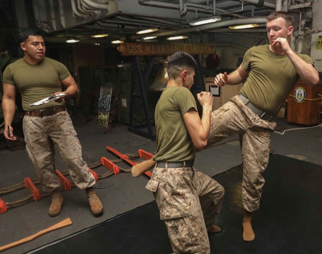 U.S. Marine Sgt. Michael Romero, left, a satellite operator with the 22nd Marine Expeditionary Unit, looks on as Marines execute a counter-to-the-round kick technique during a Marine Corps Martial Arts Program test in the well deck of the Wasp-class amphibious assault ship USS Kearsarge. Sgt. Romero evaluated the Marines, both with Combat Logistics Battalion 22, on their understanding and performance of grey and green belt MCMAP techniques. Marines and Sailors with the 22nd MEU and Kearsarge Amphibious Ready Group are deployed to the 5th Fleet area of operations in support of naval operations to ensure maritime stability and security in the Central Region, connecting the Mediterranean and the Pacific through the western Indian Ocean and three strategic choke points. (U.S. Marine Corps photo by Lance Cpl. Tawanya Norwood)