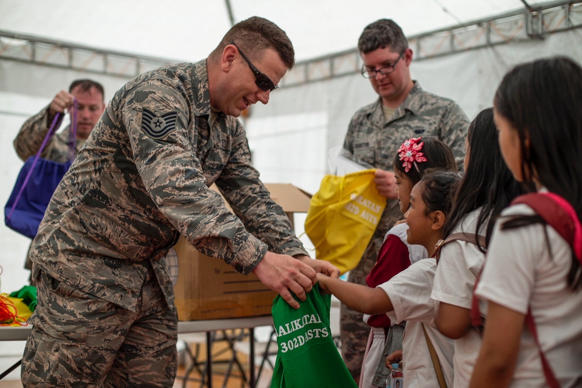 A smiling airman passes a bag to a student, who smiles up at him.