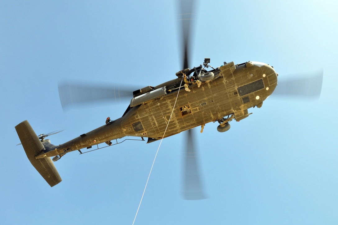 A service member looks down from a helicopter while holding a hoisting rope.