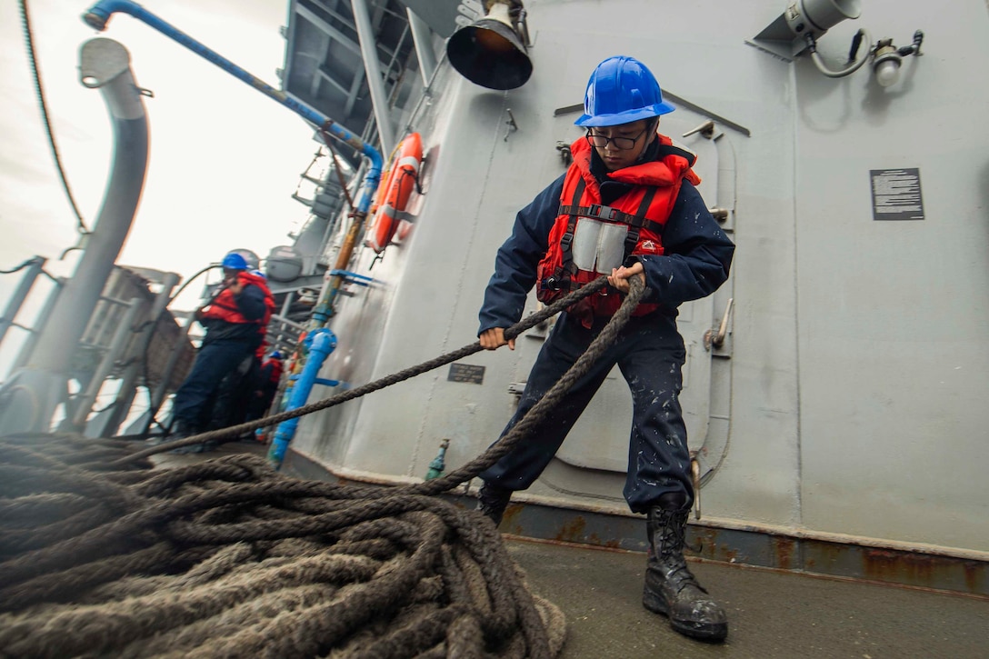 A sailor pulls a rope with a sailor working behind.