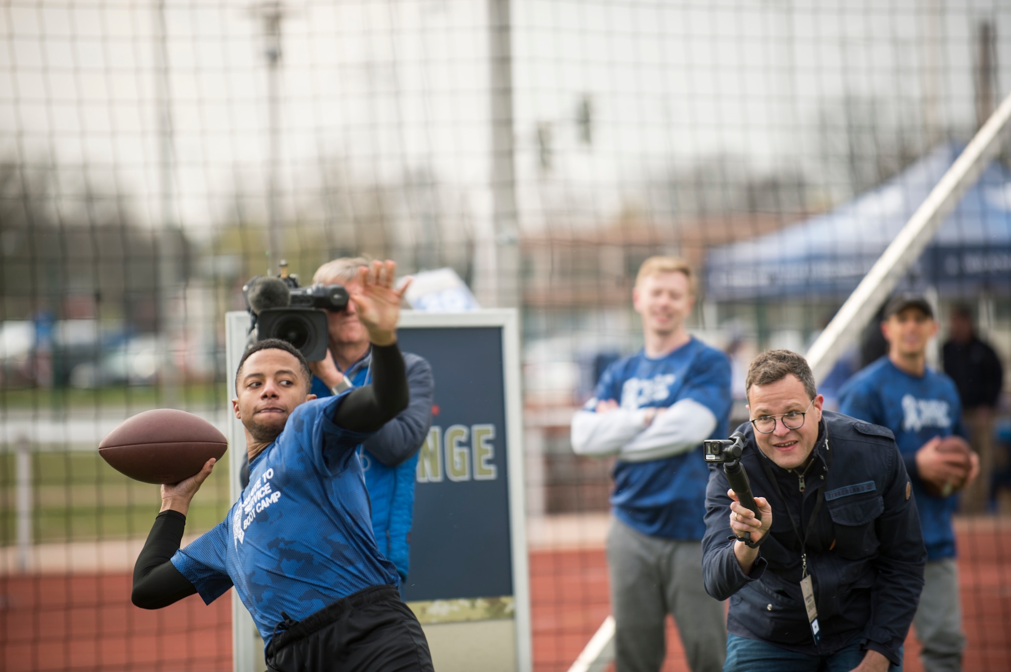 An Alejandro Villanueva football camp attendee throws a football while NBC Europe videographers film during a football distance throw drill at Kaiserslautern High School on Vogelweh Military Complex, Germany, April 13, 2019. Villanueva, Pittsburgh Steelers offensive lineman, served in the U.S. Army before becoming a professional football player. (U.S. Air Force photo by Staff Sgt. Jonathan Bass)