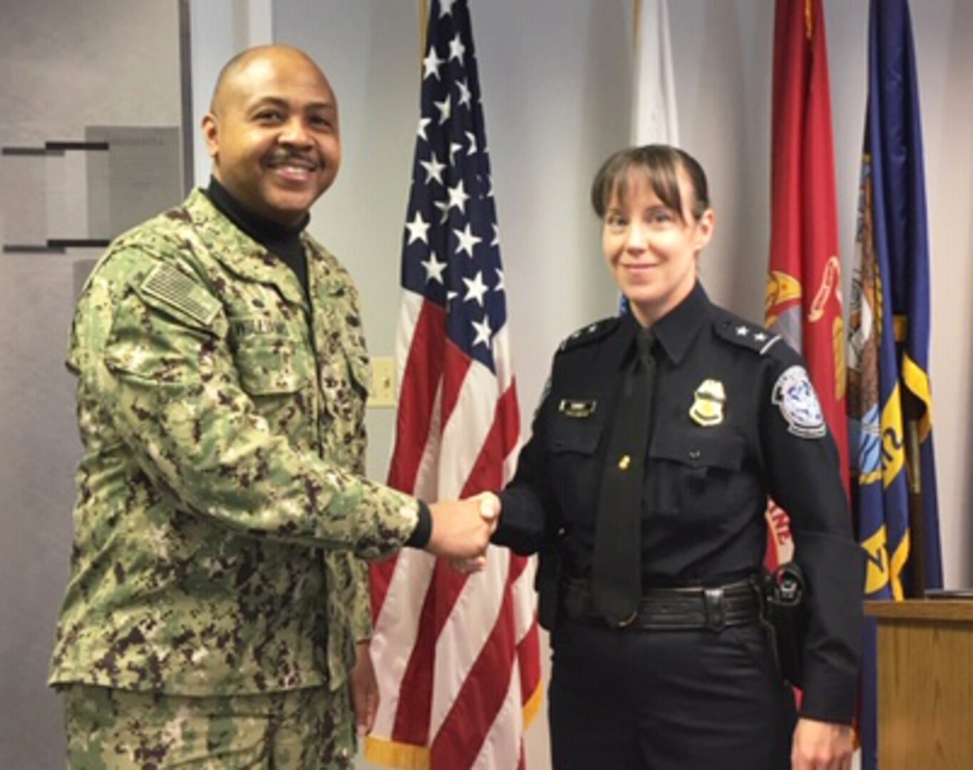 A Navy military officer shakes hands with a civil servant wearing a black Customs and Border Protection uniform