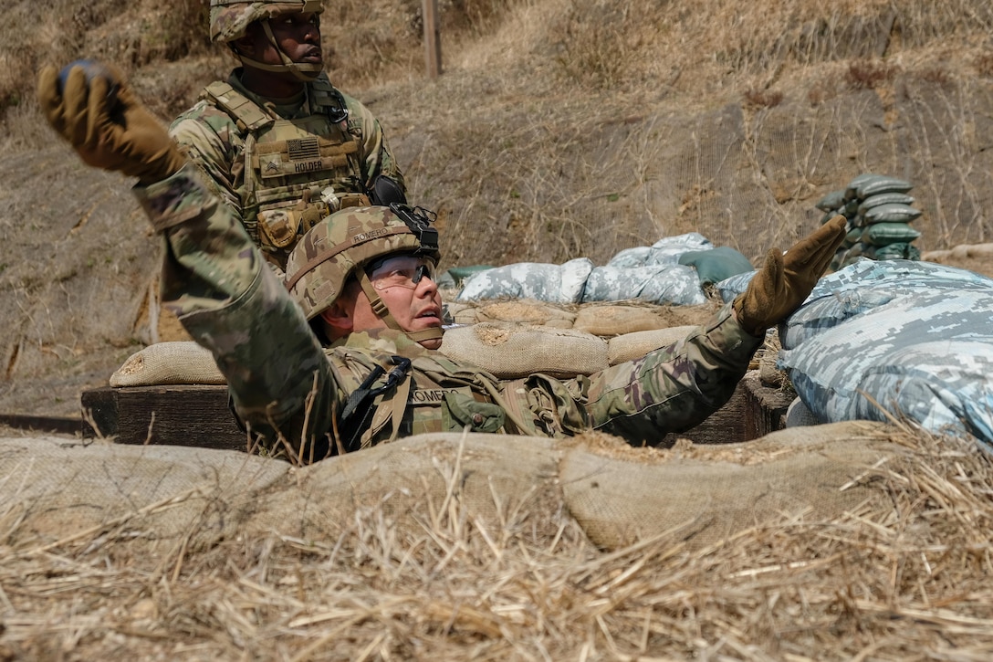 A soldier in a hole throws a training hand grenade.