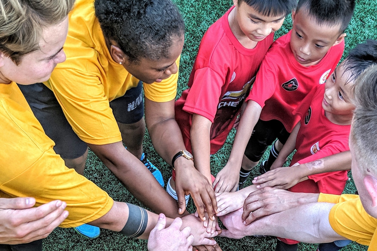 Sailors huddle with children during a soccer game.