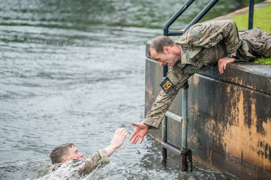 A soldier reaches to help another soldier out of the water.