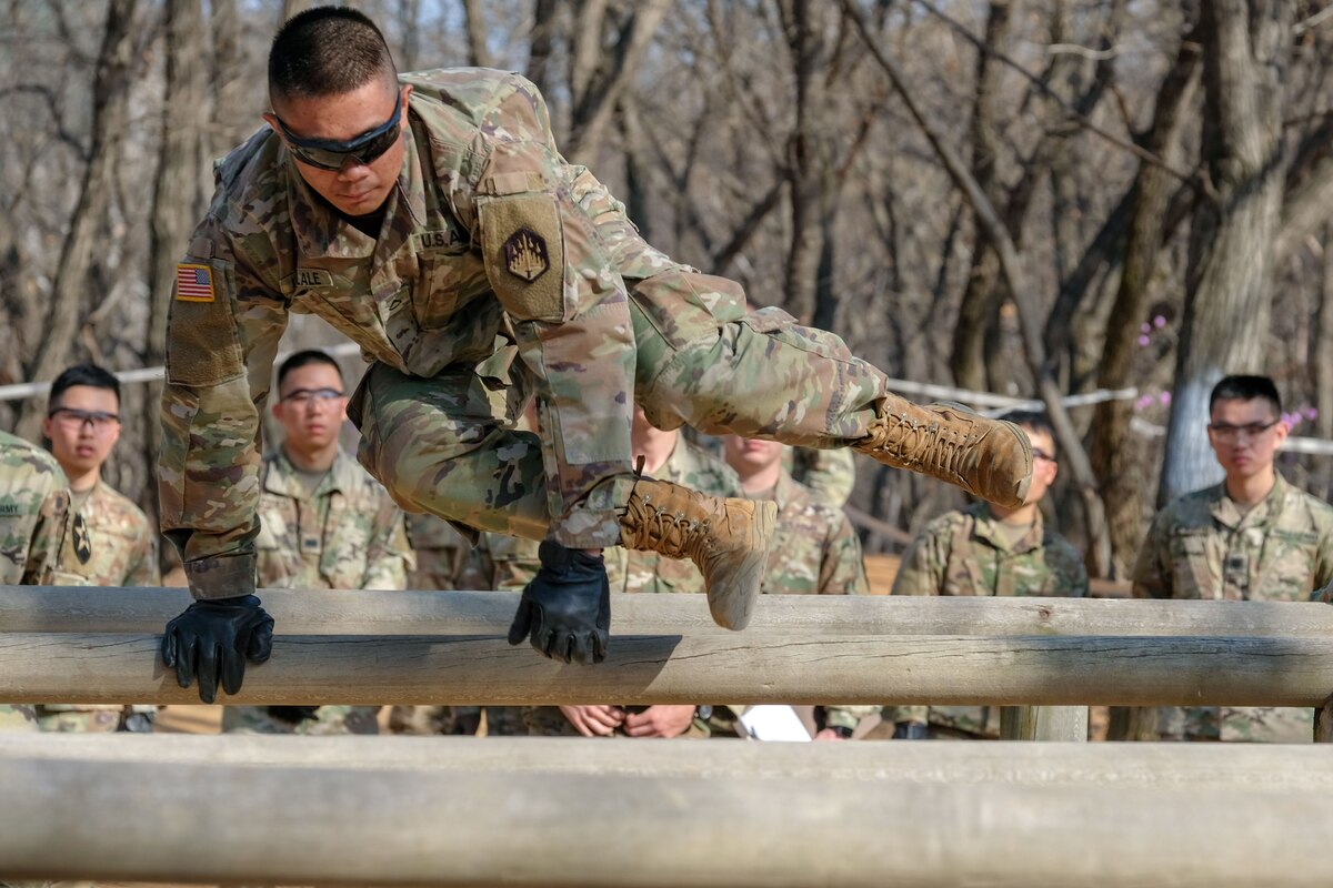 A soldier jumps over a wooden obstacle during a competition.