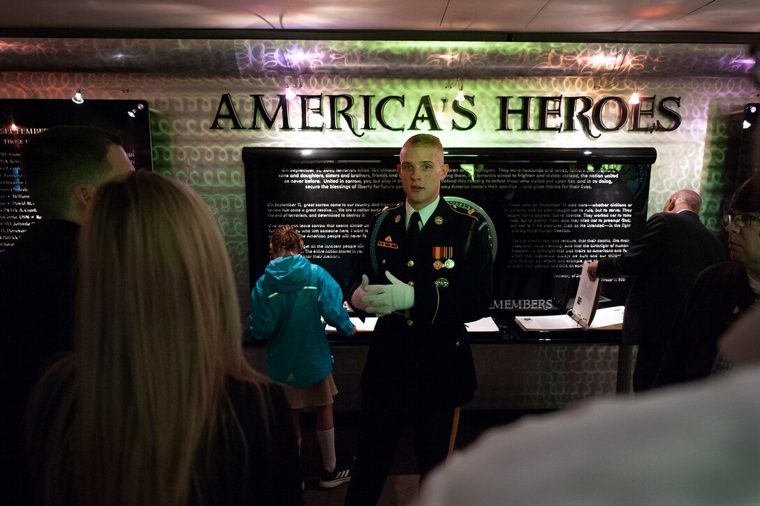 A soldier stands in front of a display that reads “America’s Heroes.”