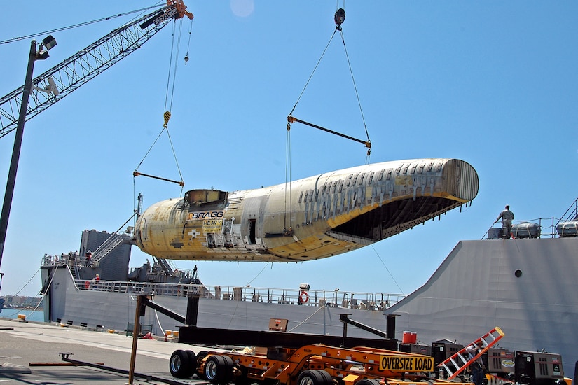 A crane lifts a fuselage to a ship.