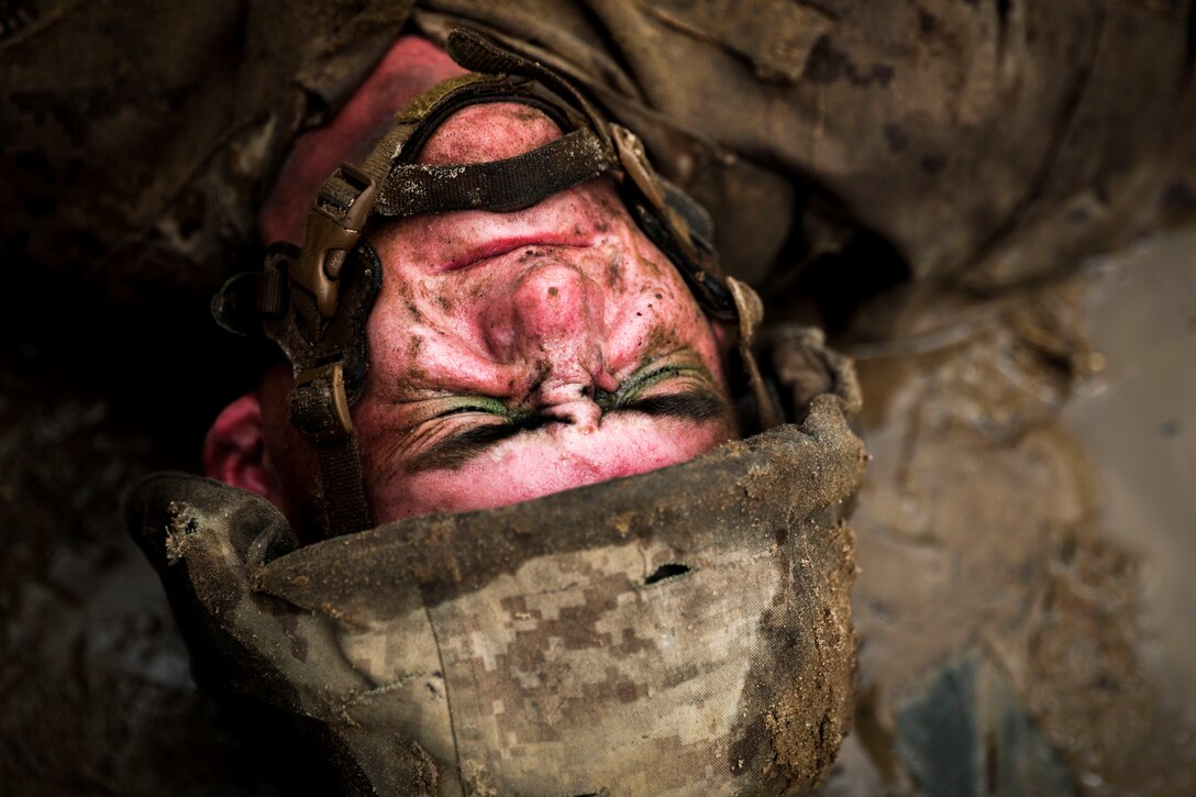 A Marine grimaces as he lays face-up in the sand.
