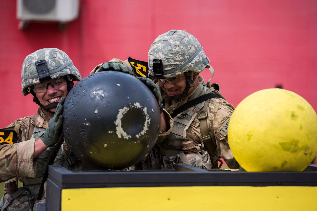 Two airmen position a large ball onto a platform.