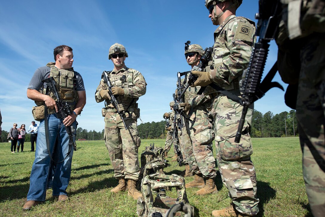 NASCAR driver Ryan Newman speaks with a group of soldiers on a grassy field.