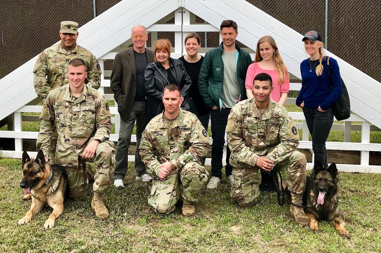 Civilians, soldiers and two military working dogs pose for a group photo.