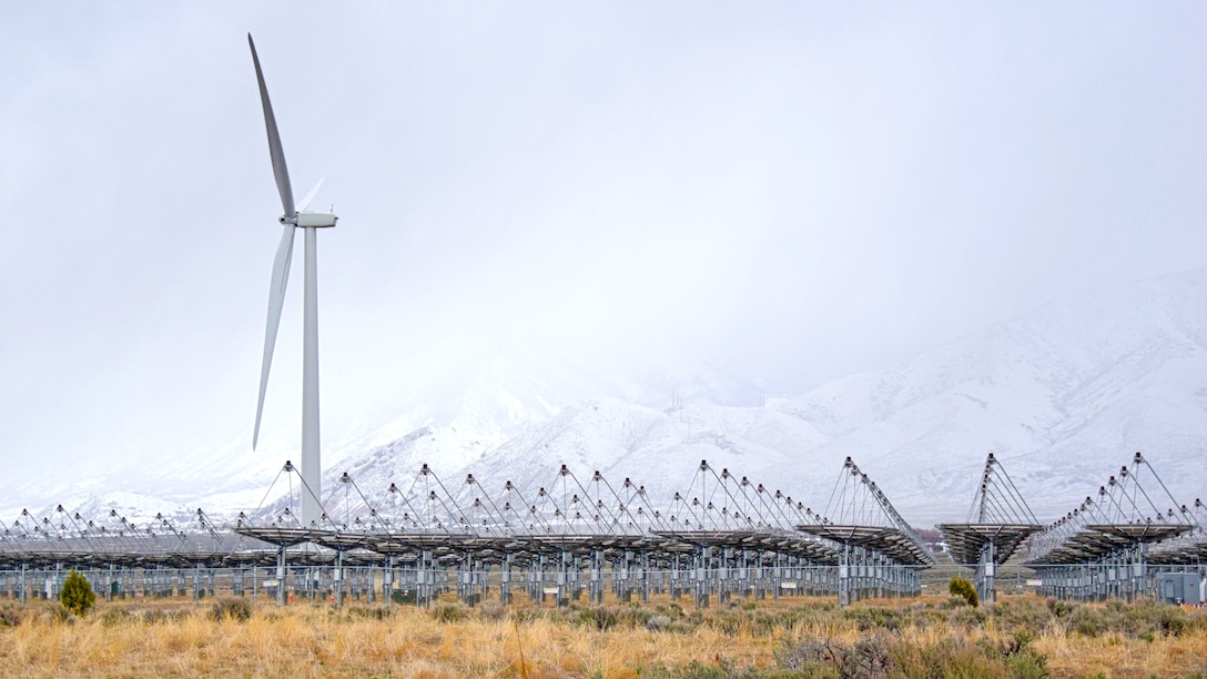 A wind turbine and solar arrays grace desert.