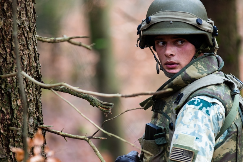 A soldier in the woods looks rearward.