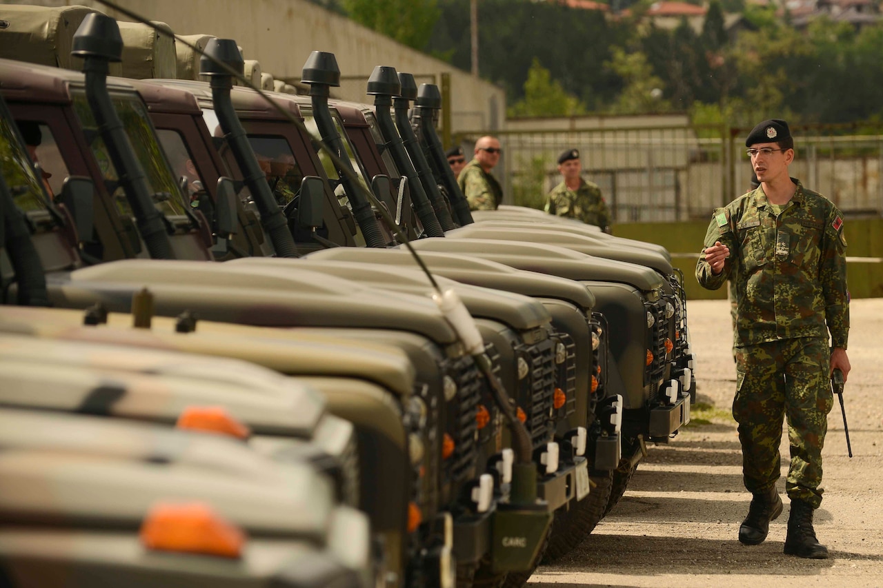 An Albanian service member walks alongside military vehicles.