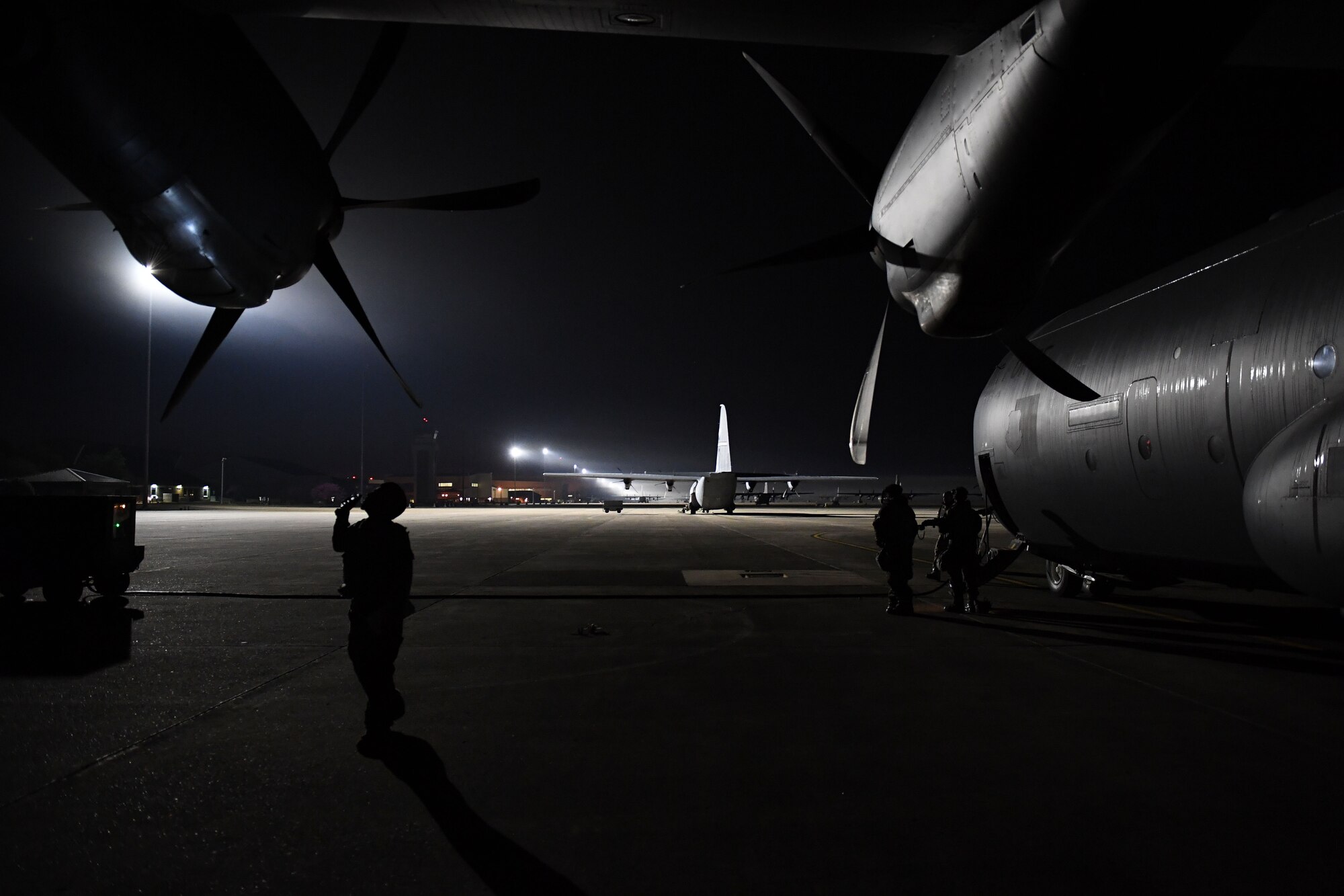An Airman uses a flashlight at night to inspect a C-130J.