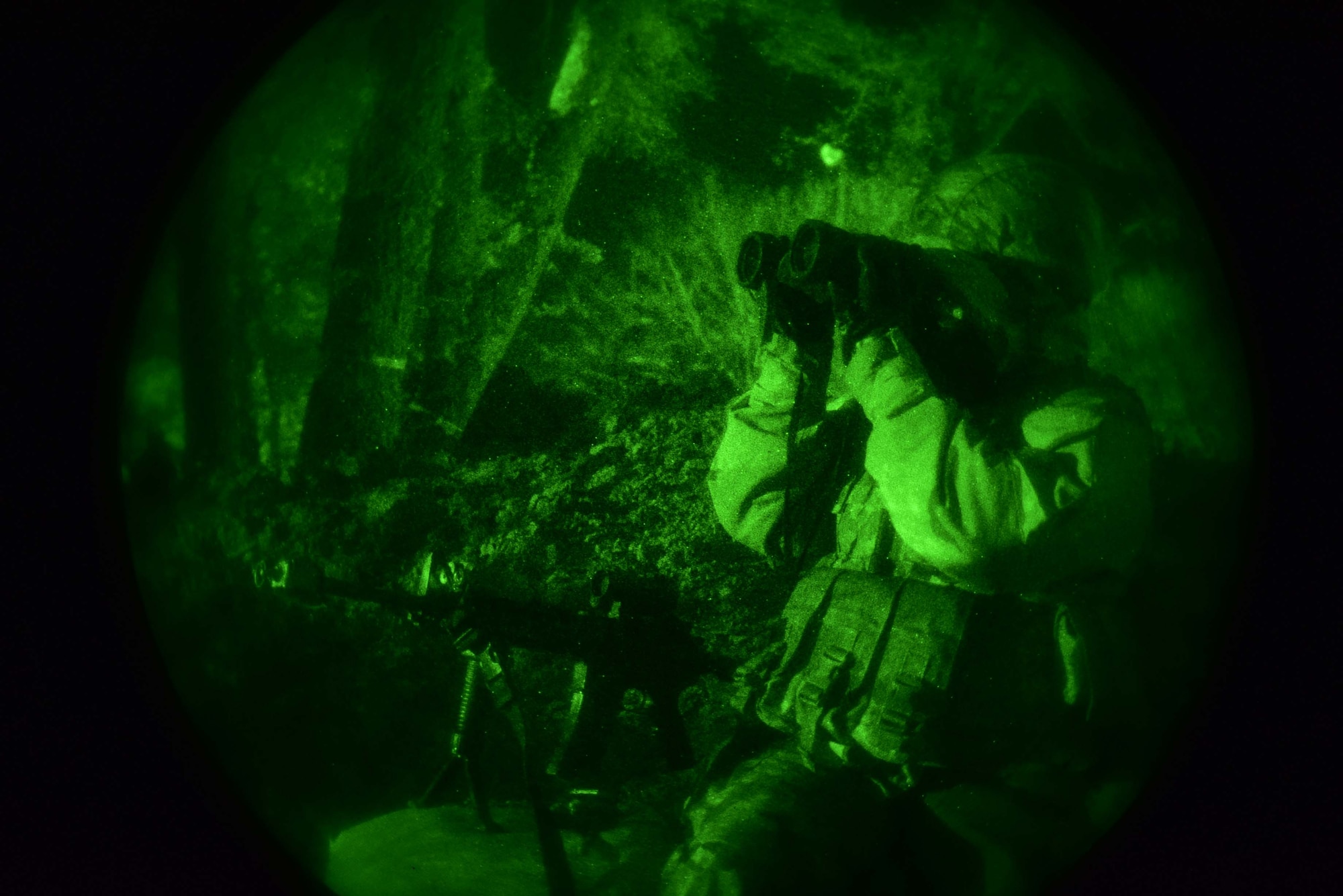 An Airmen looks through binoculars at night