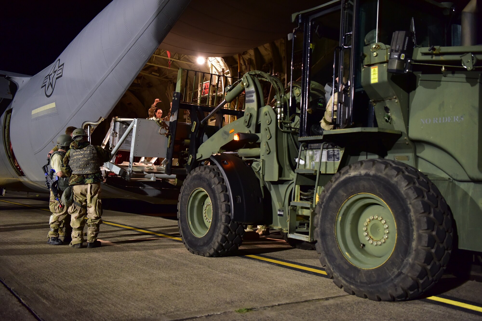 Airmen load equipment on the back of a C-130J at night
