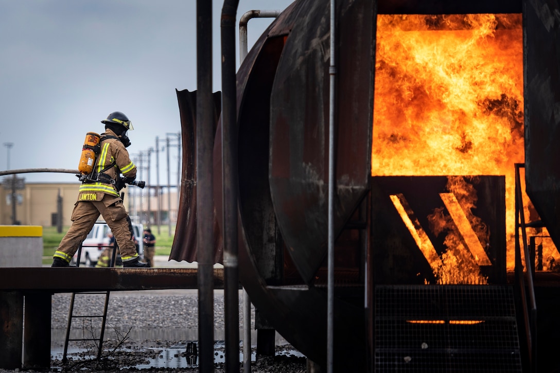 A firefighter holding a hose stands outside a burning fuselage during training.