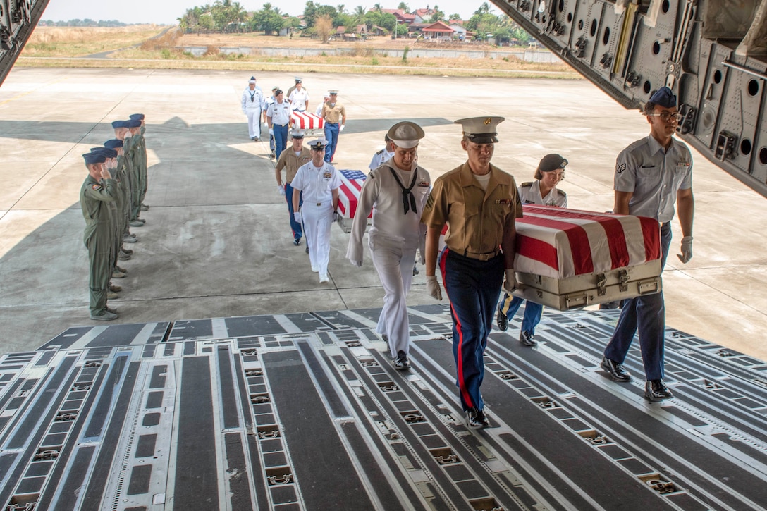 Service members carry coffins into an aircraft.