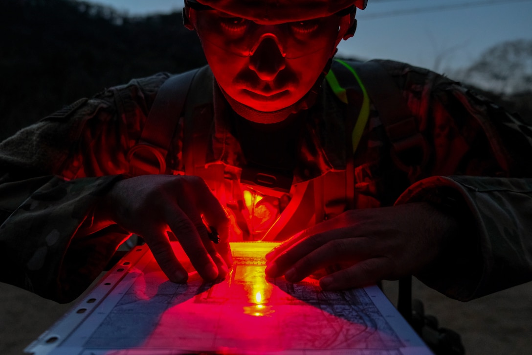 A soldier uses a red lens flashlight to look at a map in the dark.