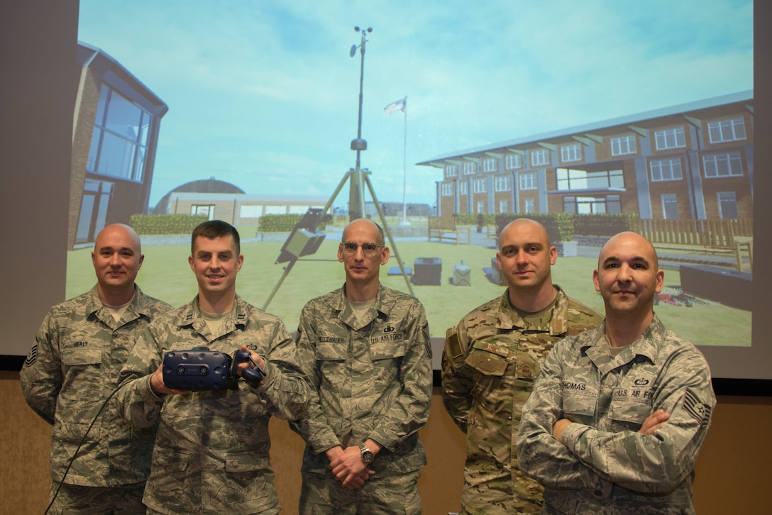 Airmen from the 1st Weather Group pose for a group photo in front of a projection of a new virtual reality training system March 14, 2019, at Offutt Air Force Base, Nebraska. The VR trainer uses off-the-shelf computing hardware, making it easier for other units that wish to adopt the technology. (U.S. Air Force photo by Paul Shirk)