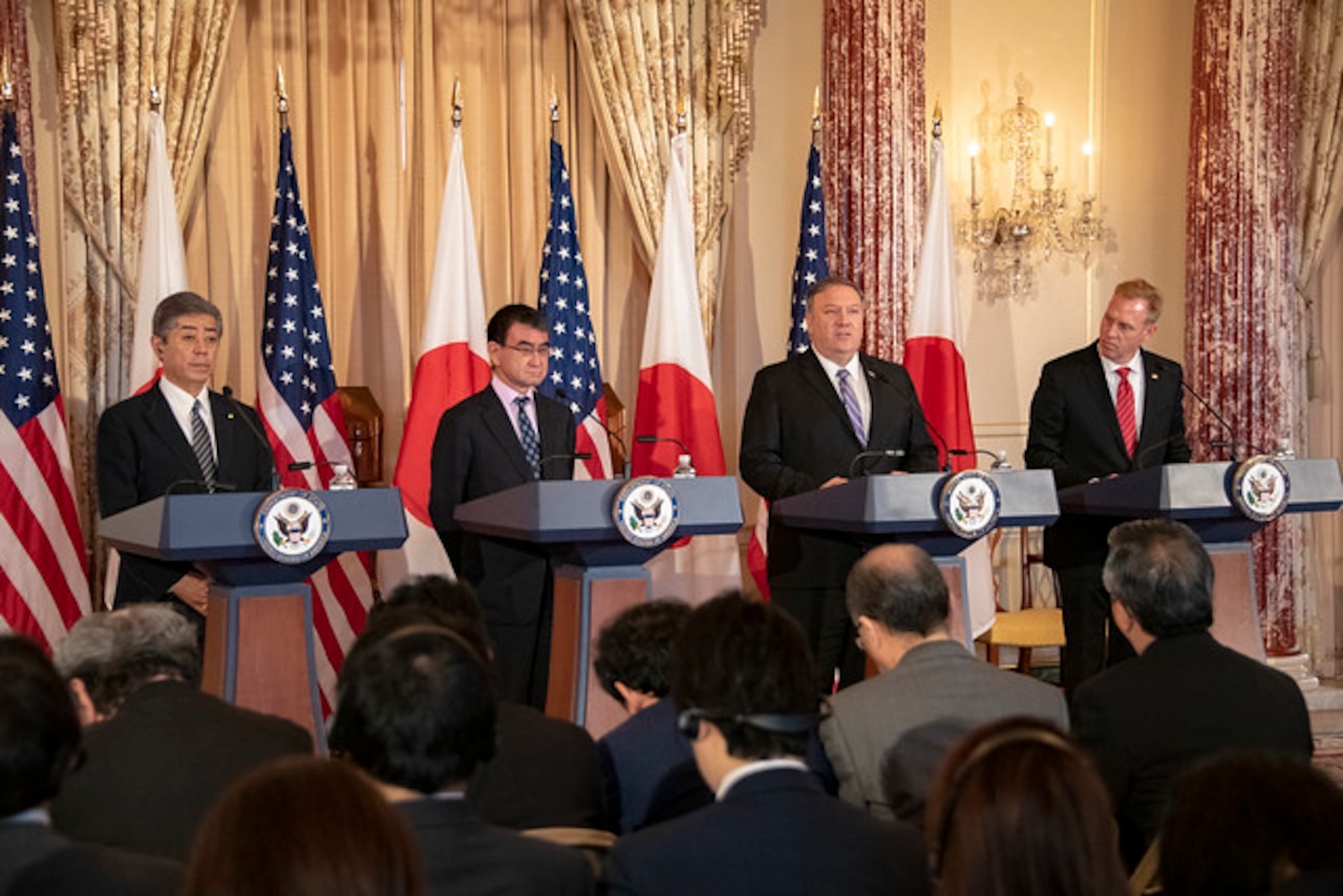 Acting Defense Secretary Patrick M. Shanahan, Secretary of State Michael R. Pompeo and two Japanese leaders stand at four different podiums in a row facing a seated crowd.