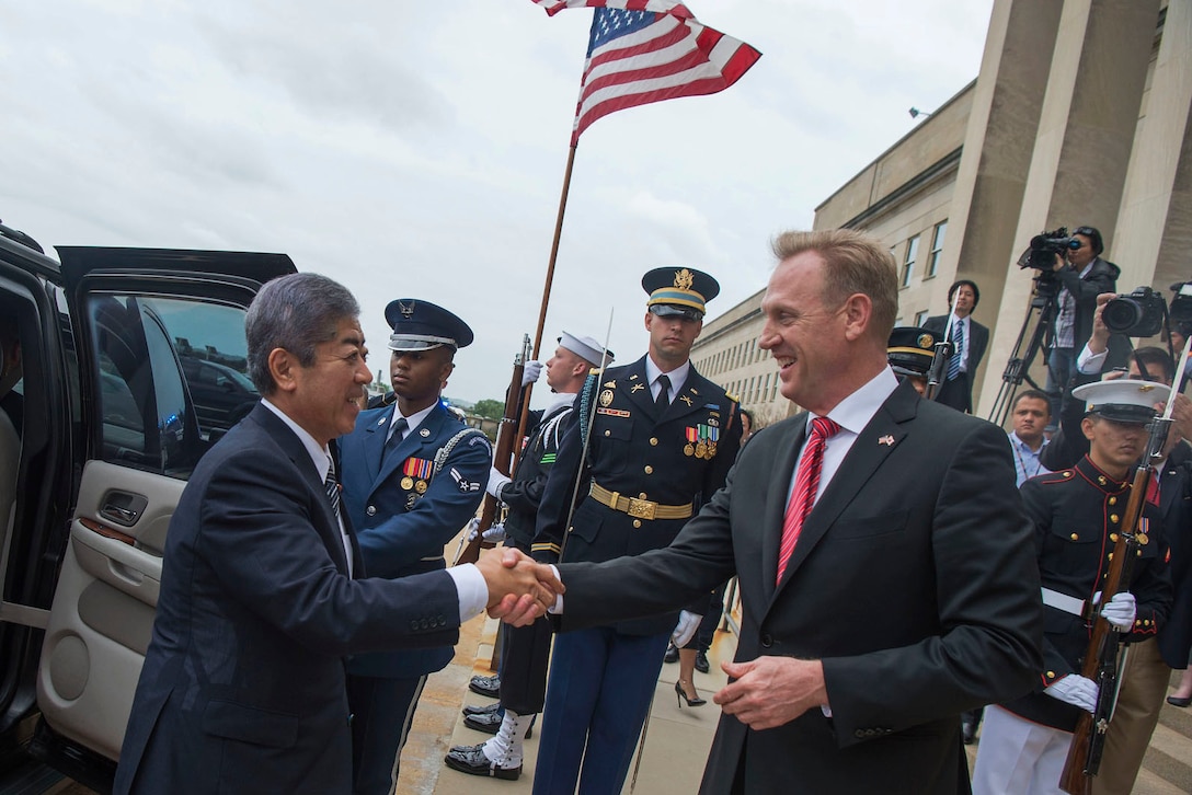 Acting Defense Secretary Patrick M. Shanahan shakes hands with the Japanese defense minister with service members in the background.
