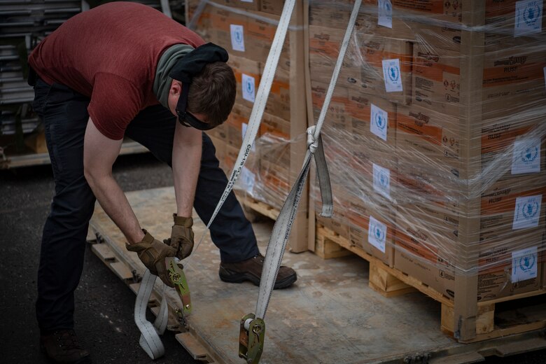 A U.S. military member supporting Combined Joint Task Force-Horn of Africa uses a ratchet strap to secure Plumpy Sup Aid to a pallet in Maputo, Mozambique, April 2, 2019. The task force is helping meet requirements identified by the United States Agency for International Development (USAID) assessment teams and humanitarian organizations working in the region by providing logistics support and manpower to USAID at the request of the Government of the Republic of Mozambique. (U.S. Air Force Photo by Tech. Sgt. Chris Hibben)