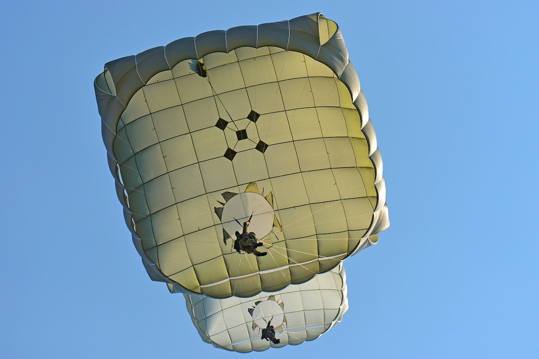Two soldiers, shown from beneath with their parachutes above them, descend through the sky.