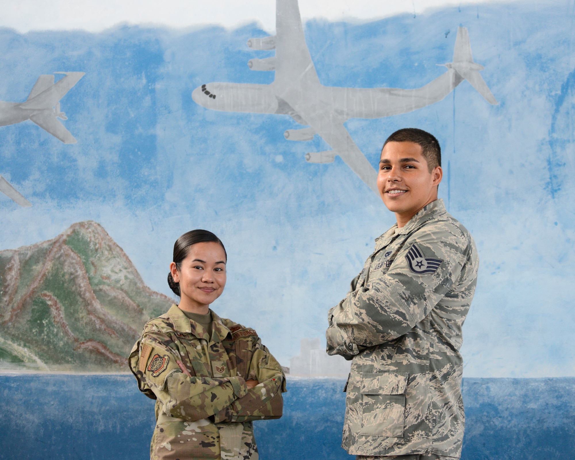 Staff Sgt. Carlyn Ramos, an integrated instument and flight control systems craftsman (left) and Staff Sgt. Nicholas Espinoza, an aircraft electrical and environmental systems technician (right), both assigned to the 735th Air Mobility Squadron, pose in front of a mural inside Hangar No. 9 at Joint Base Pearl Harbor-Hickam, Hawaii April 16, 2019. The 735th Air Mobility Squadron ensures incoming aircraft can complete their missions in the Pacific region. (U.S. Air National Guard photo by Staff Sgt. Steven Tucker)