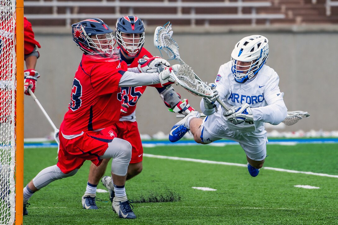 Three athletes chase a ball during a lacrosse game.