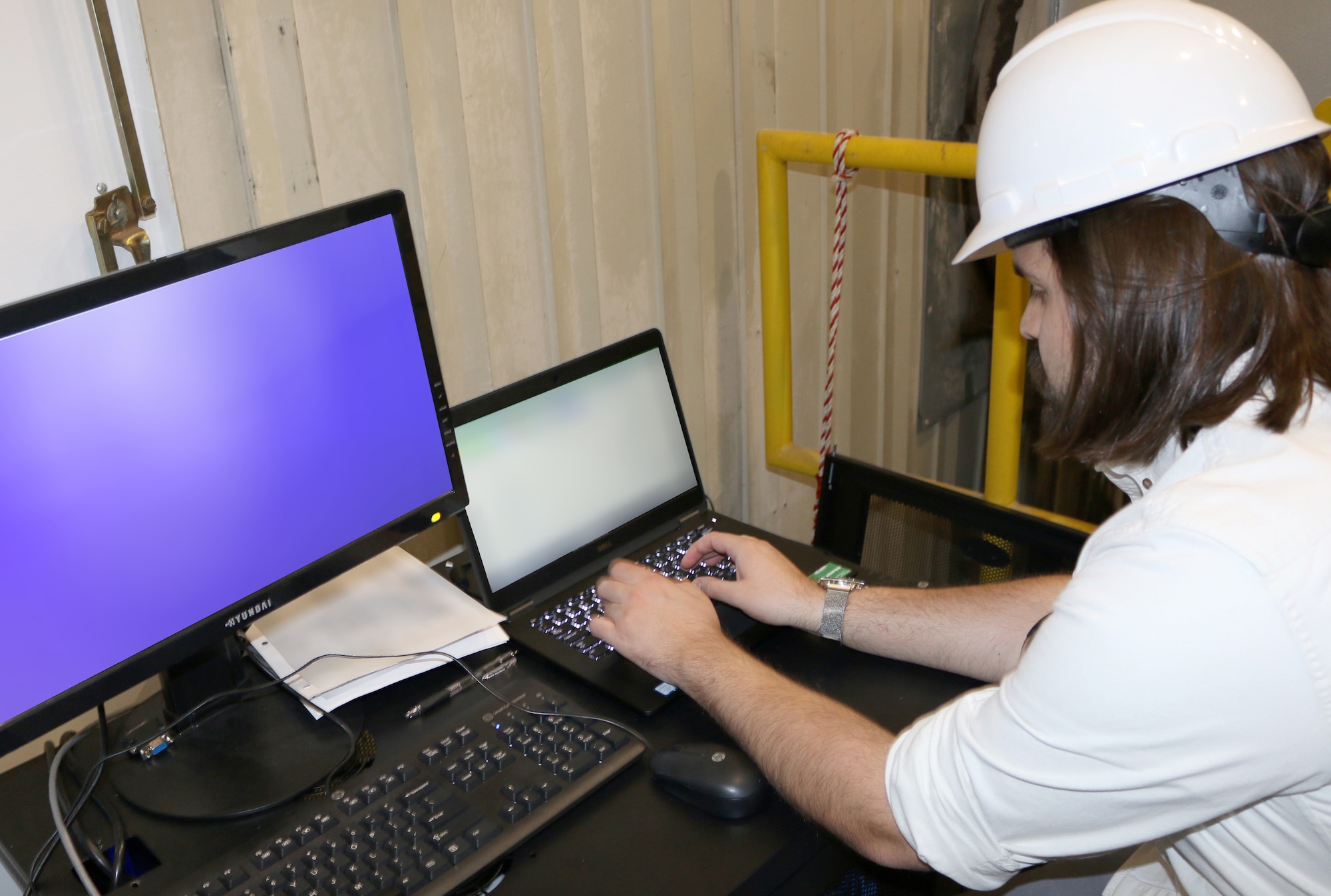 Joseph Mann, AEDC instrumentation, data and controls engineer, works at the U7 portable data station in one of the arc-heated test cells at Arnold Air Force Base. Members of the Test Support System Division at Arnold AFB designed and built the portable data acquisition system to setup and prepare instrumentation between and during testing. (U.S. Air Force photo by Deidre Ortiz) (This image has been altered for security purposes)