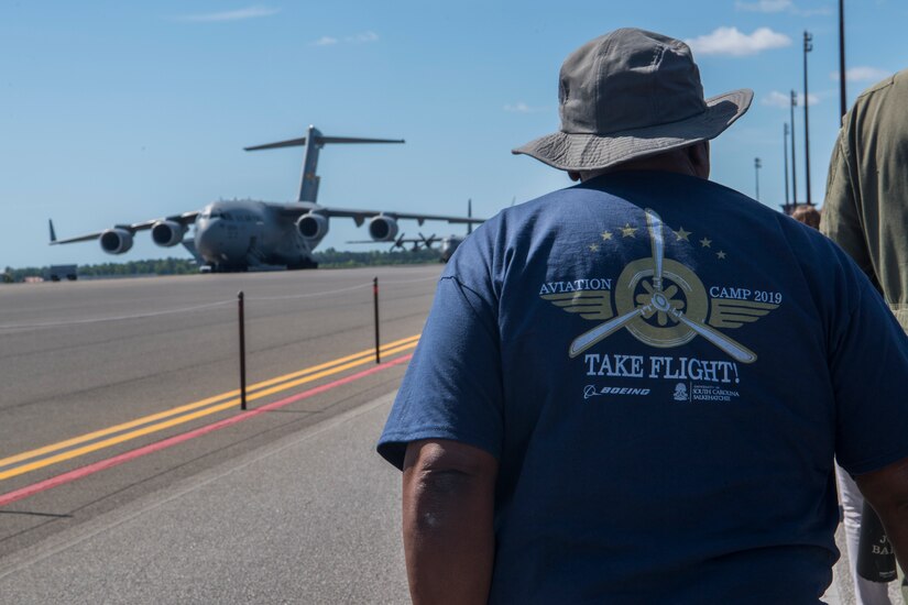 A chaperone for the Take Flight Aviation Camp walks towards a C-17 Globemaster III April 18, 2019, at Joint Base Charleston, S.C.