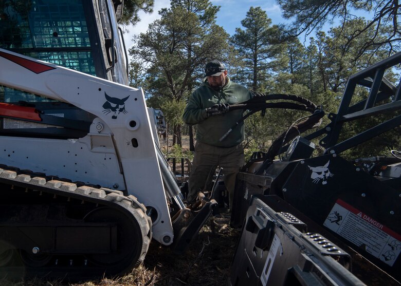 Richard Chaves, fire operations technician, attaches a mastication machinery to a bulldozer at Kirtland Air Force Base, N.M., April 16, 2019. Kirtland is conducting a multi-step wildfire prevention project spanning across 16,000 acres of its eastern-most remote forest area. (U.S. Air Force photo by Staff Sgt. J.D. Strong II)