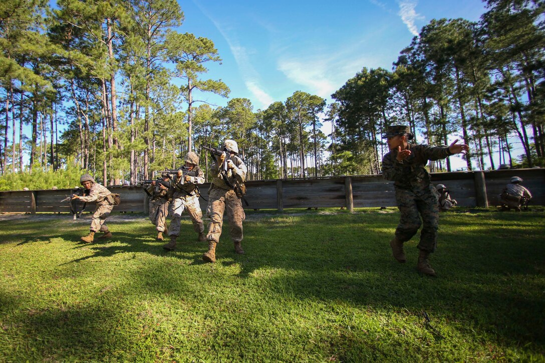 A drill sergeant instructs several Marine Corps recruits on a field holding rifles.