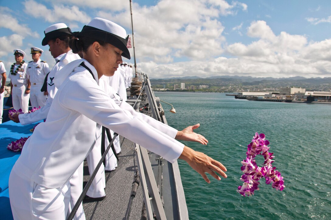 A sailor drops a lei into the ocean from the deck of a ship.