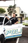 Police officer stands outside door of a police car.