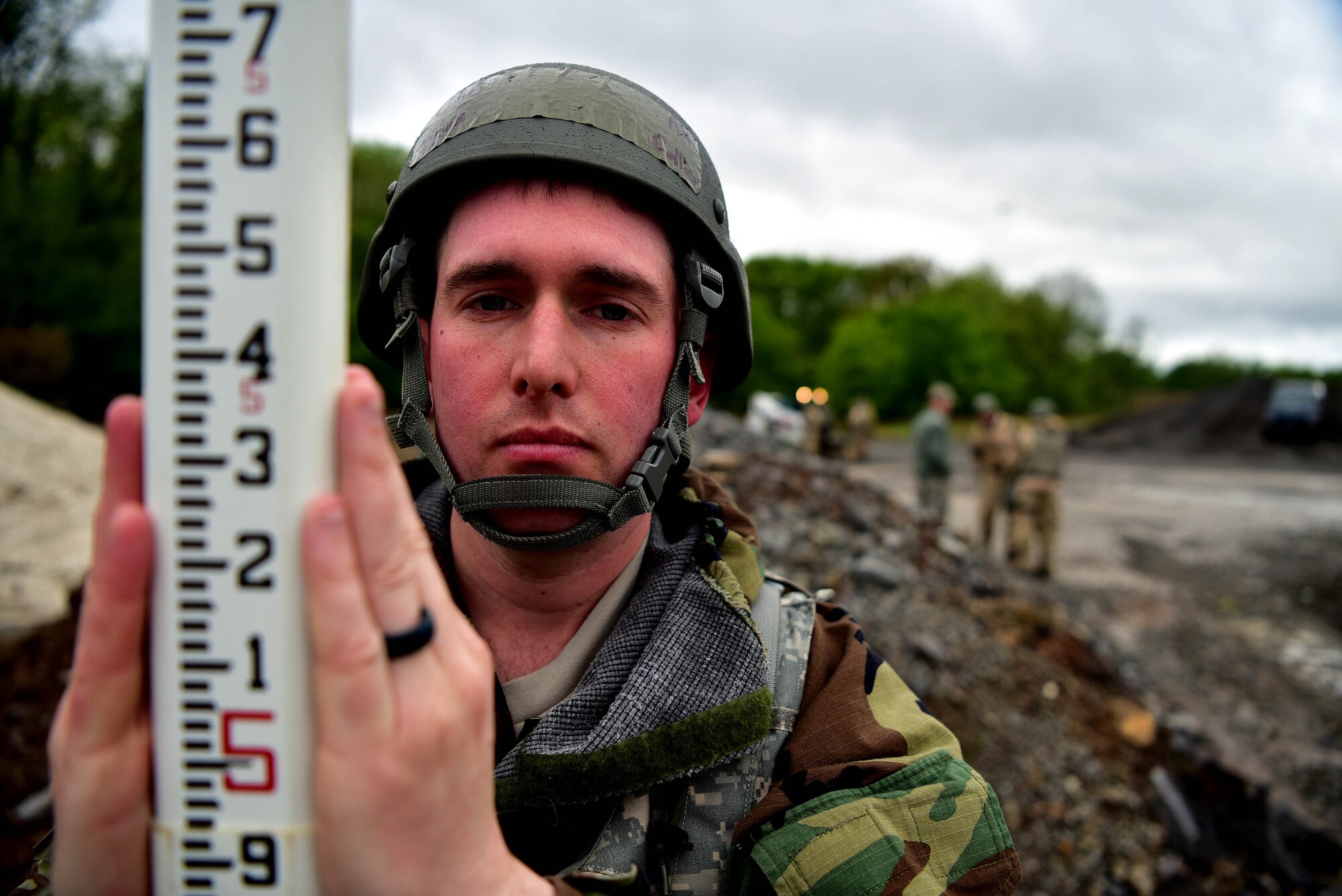 A man wearing a helmet and a pole with numbers on it look sinto the camera.