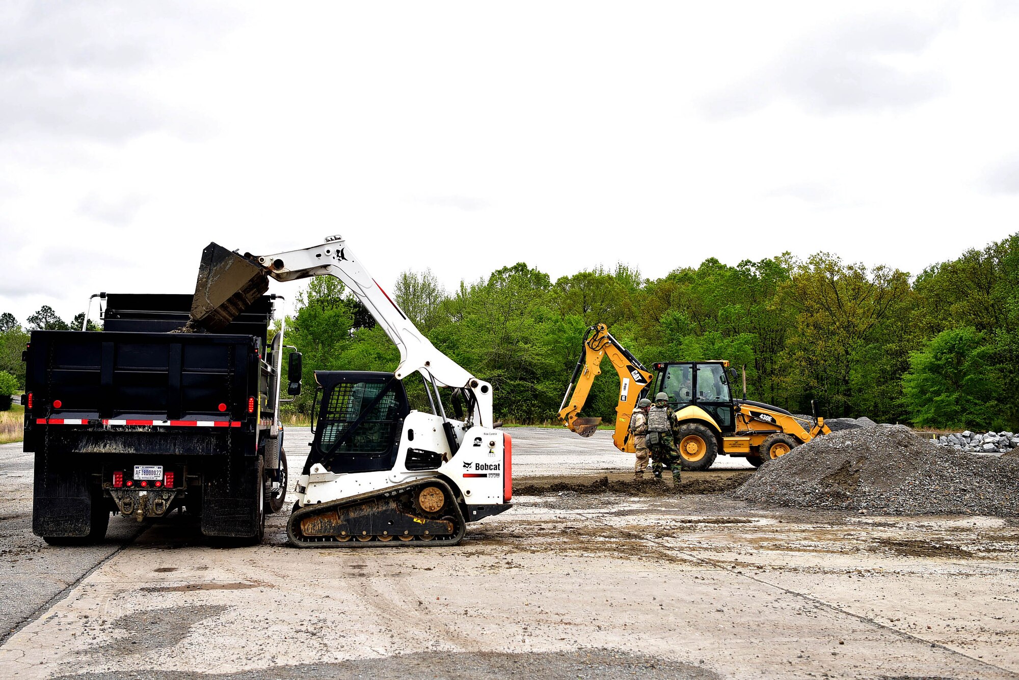 Two pieces of machinery pick up debris from a hole in the ground.