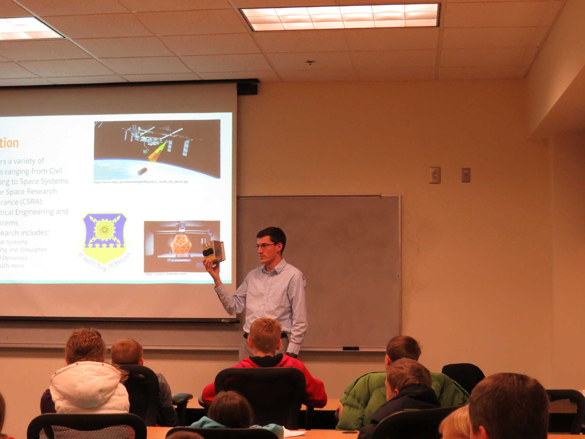 Air Force Institute of Technology astronautical engineering graduate student, William Gallagher shows local STEM students interested in space an example of CubeSat hardware from the Center for Space Research and Assurance.  The mission shown is scheduled to launch in 2019.  CSRA is currently developing a space-qualified 6U CubeSat bus, or a space vehicle designed to carry a variety of different mission payloads to support hands-on student education and research.  The bus will be designed with the ability to upload new flight and payload software while on-orbit. (U.S. Air Force photo/Jaclyn Knapp)
