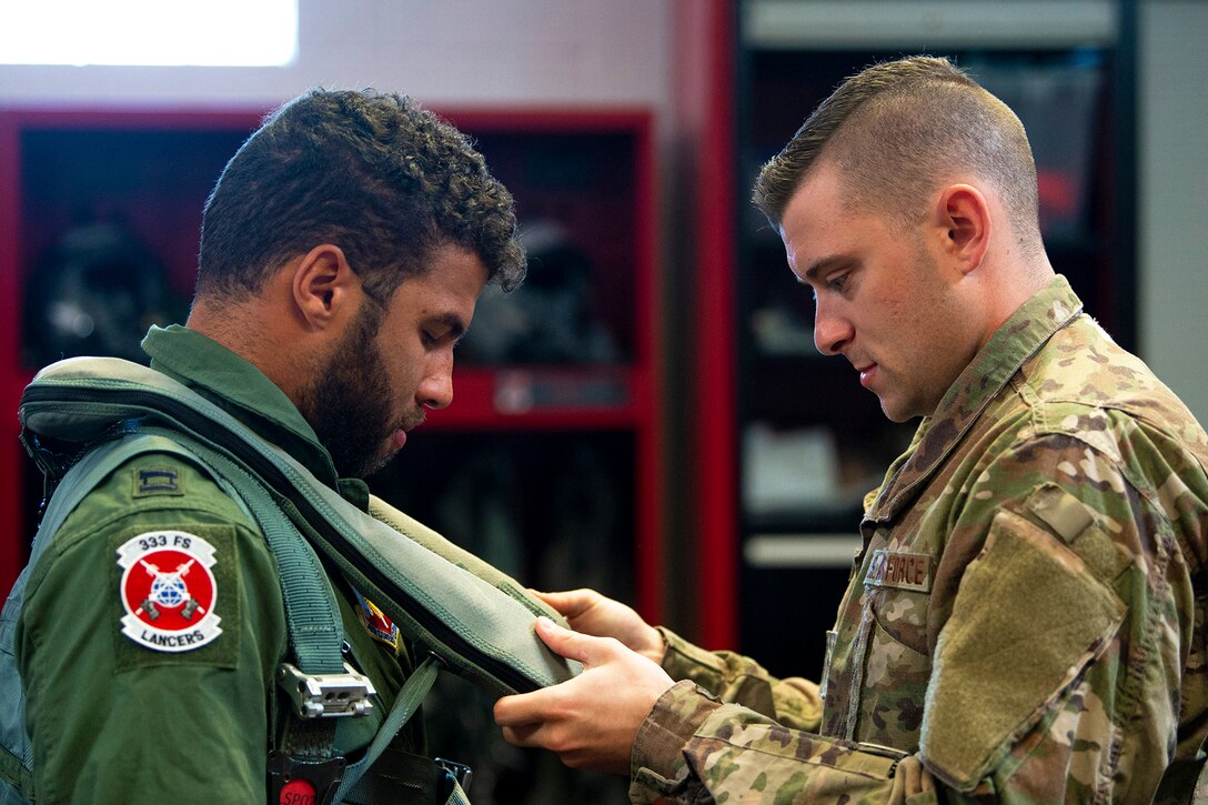 An airman adjusts a vest on a man wearing pilot's uniform.