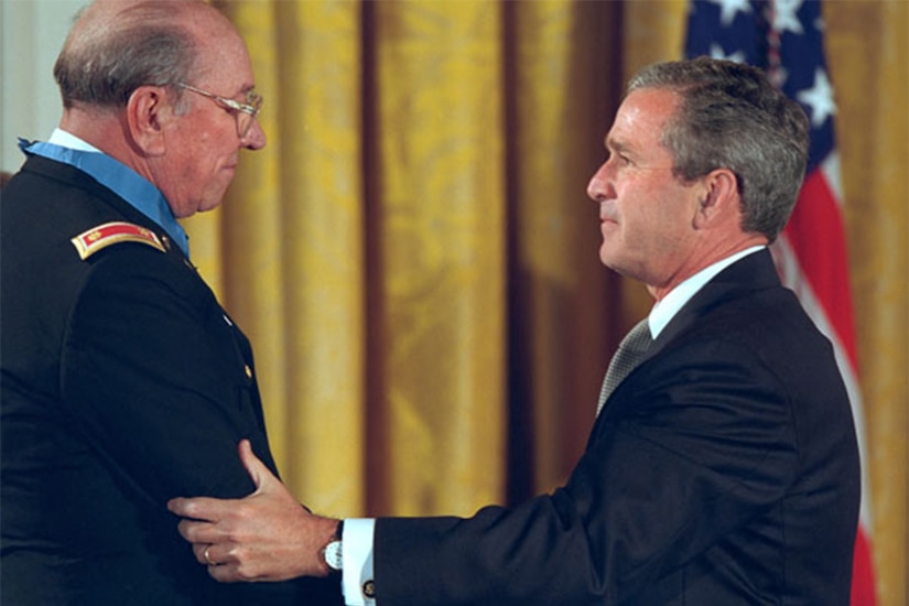President George W. Bush holds the elbow of an older soldier wearing the Medal of Honor.