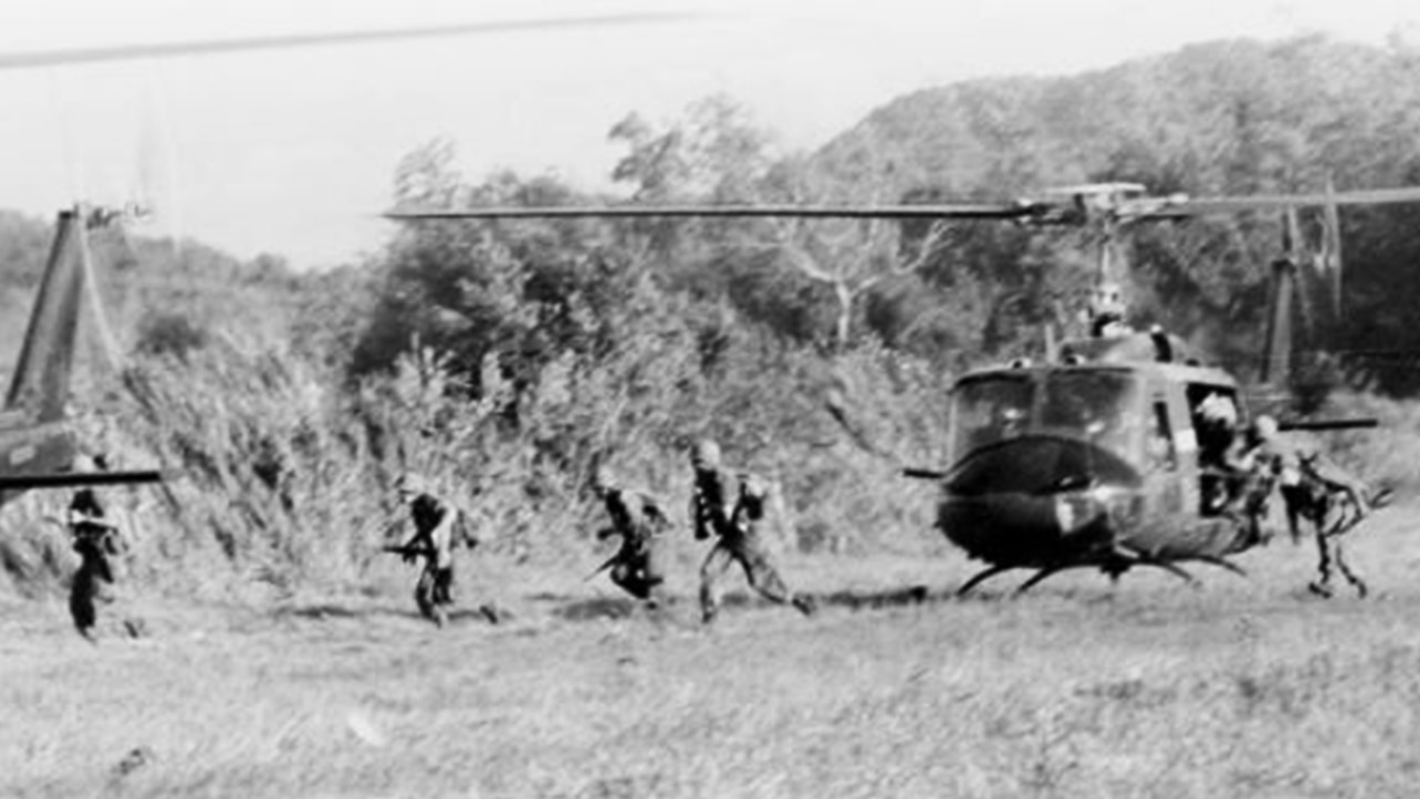 Several soldiers jump out of a helicopter in a field in Vietnam.