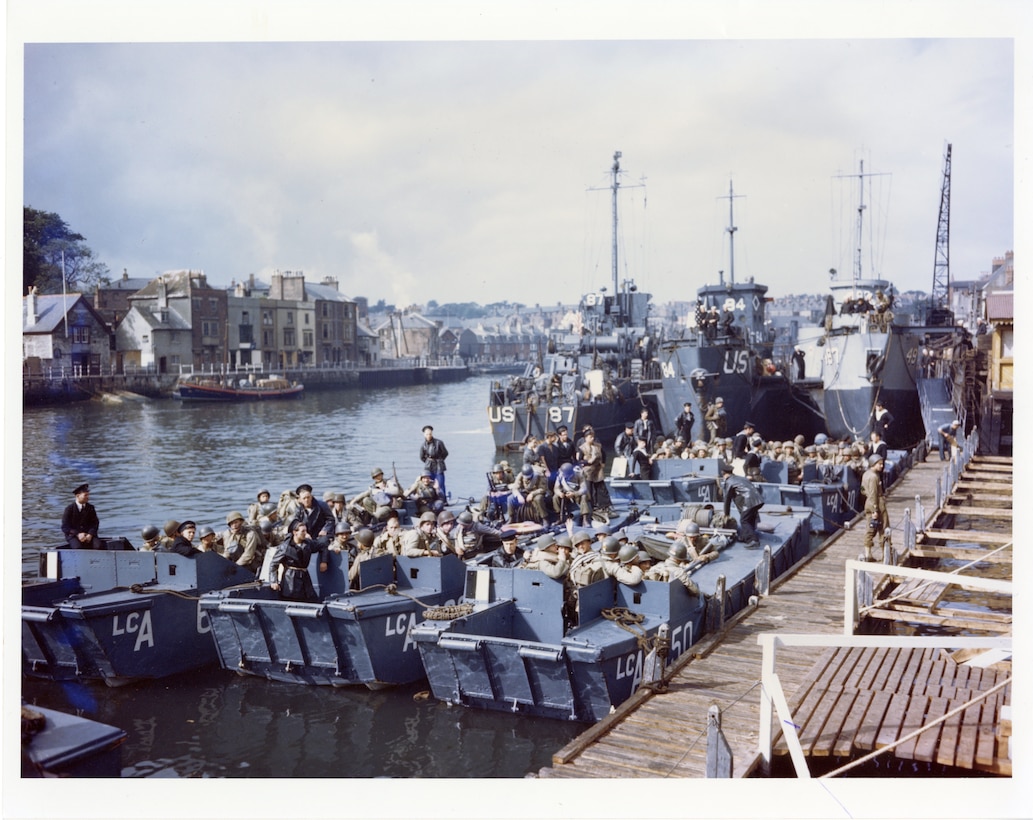 Color photo of troops in Landing Crafts with LCI(L)-84 and other naval vessels in the background.